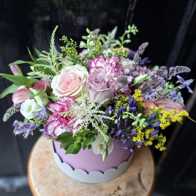 Lavender Elegance Hat Box - An elegant lilac scalloped hat box brimming with blush and mauve roses, frilled carnations, purple agapanthus, calla lily and golden solidago. A refined, luxurious gift.